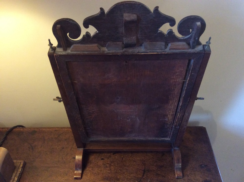 A Georgian dark mahogany skeleton toilet mirror featuring a scroll-carved cresting, rectangular pivoting mirror, side brass fixings, and trestle feet. View VIII