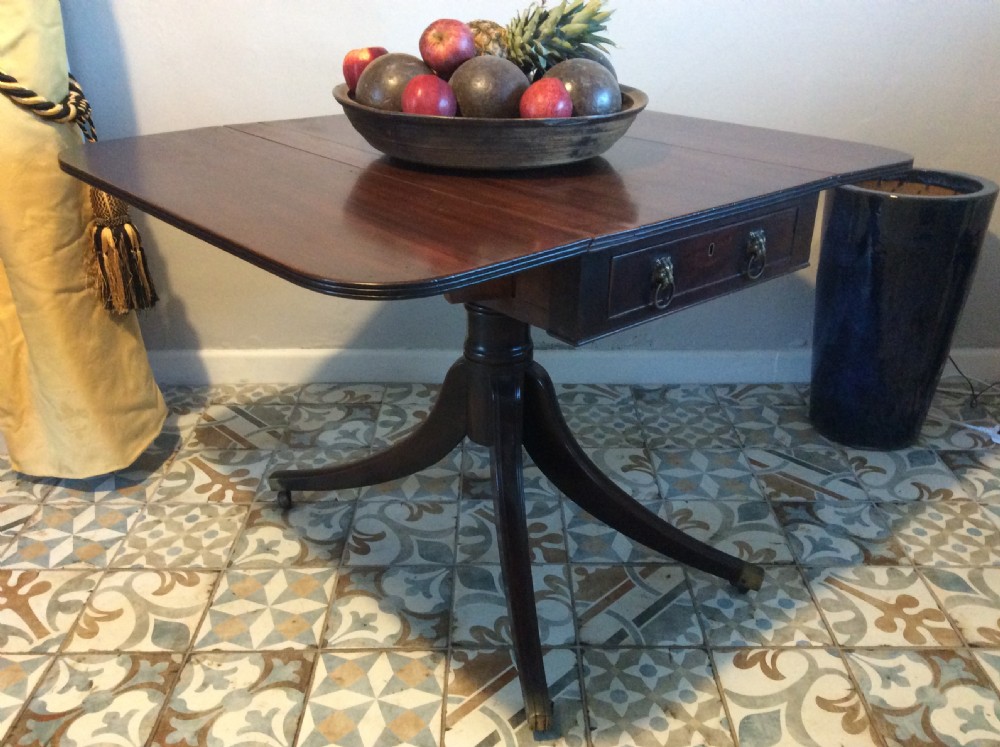 A Georgian mahogany drop-leaf hall table with two hinged side flaps, supported by a central pedestal and four curved splayed legs with brass castors. View II
