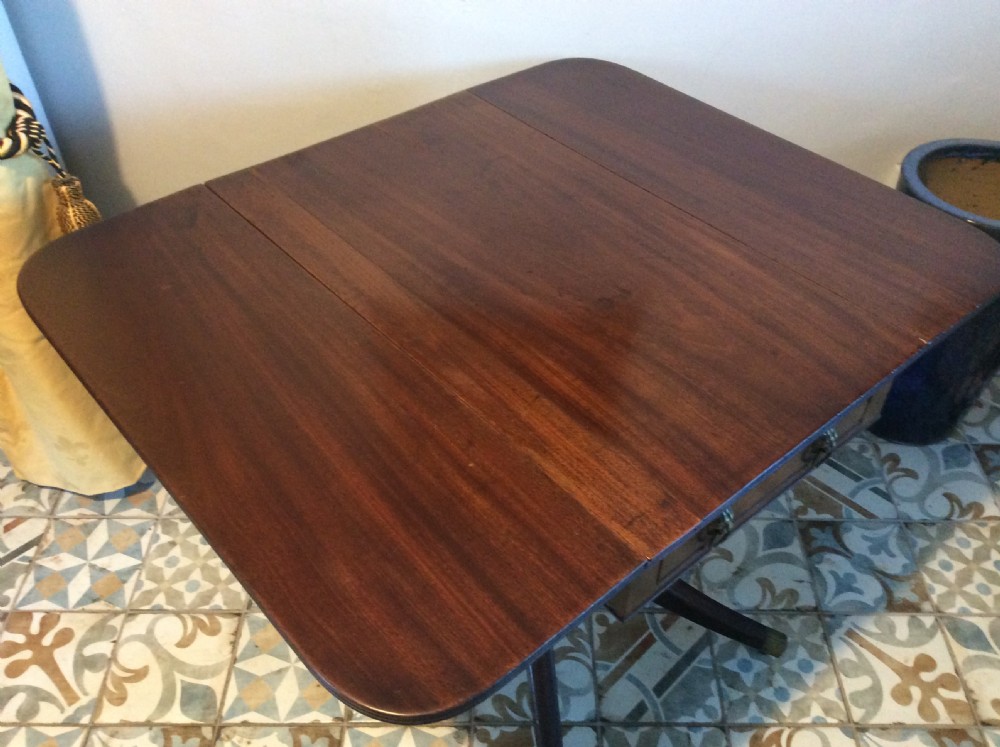 A Georgian mahogany drop-leaf hall table with two hinged side flaps, supported by a central pedestal and four curved splayed legs with brass castors. View V