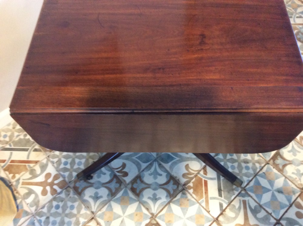 A Georgian mahogany drop-leaf hall table with two hinged side flaps, supported by a central pedestal and four curved splayed legs with brass castors. View XVI