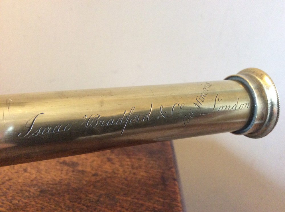 A Regency era brass multi-draw pocket telescope with a brown main barrel resting horizontally on a dark timber display stand. View III