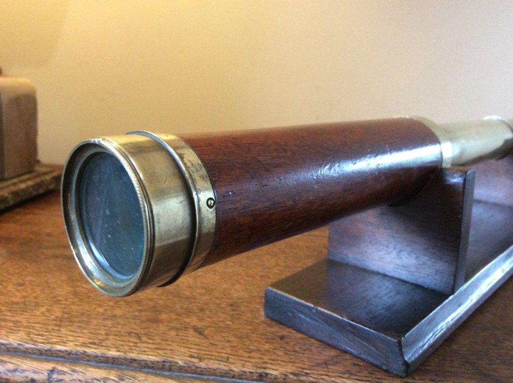 A Regency era brass multi-draw pocket telescope with a brown main barrel resting horizontally on a dark timber display stand. View V