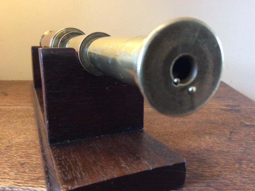 A Regency era brass multi-draw pocket telescope with a brown main barrel resting horizontally on a dark timber display stand. View IX