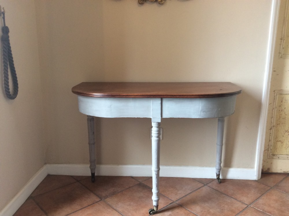 A nineteenth-century D-end console table featuring a polished dark wood top, light blue painted apron and turned legs set on brass castors.