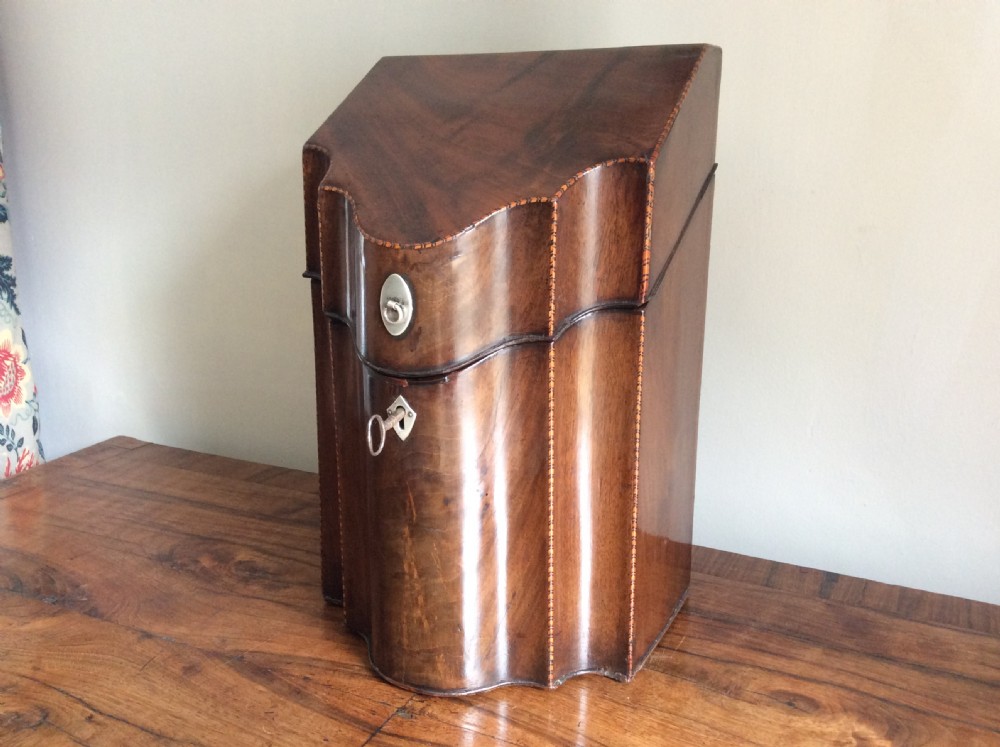 A Georgian mahogany knife box featuring a sloped hinged lid, serpentine front, boxwood stringing, and a metal keyhole escutcheon.
