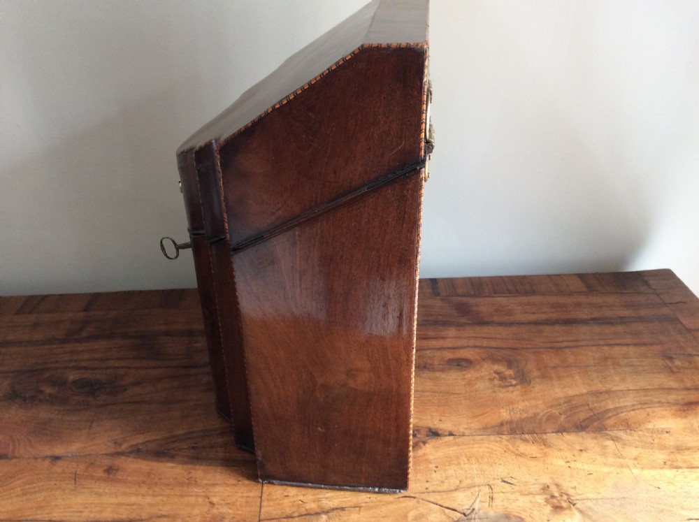A Georgian mahogany knife box featuring a sloped hinged lid, serpentine front, boxwood stringing, and a metal keyhole escutcheon. View IX