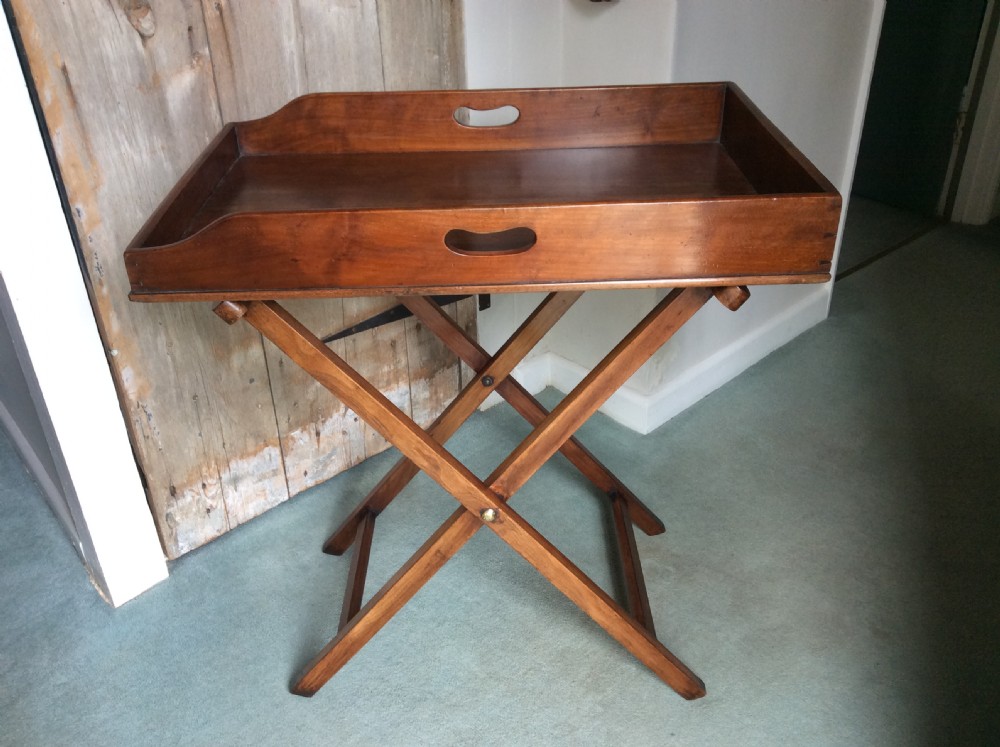 A nineteenth-century mahogany butlers tray featuring raised gallery sides with cut-out handles, resting on a folding X-frame wooden stand.