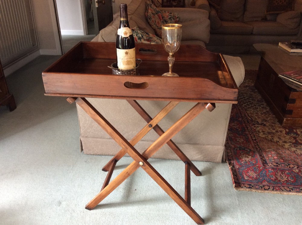A nineteenth-century mahogany butlers tray featuring raised gallery sides with cut-out handles, resting on a folding X-frame wooden stand. View II