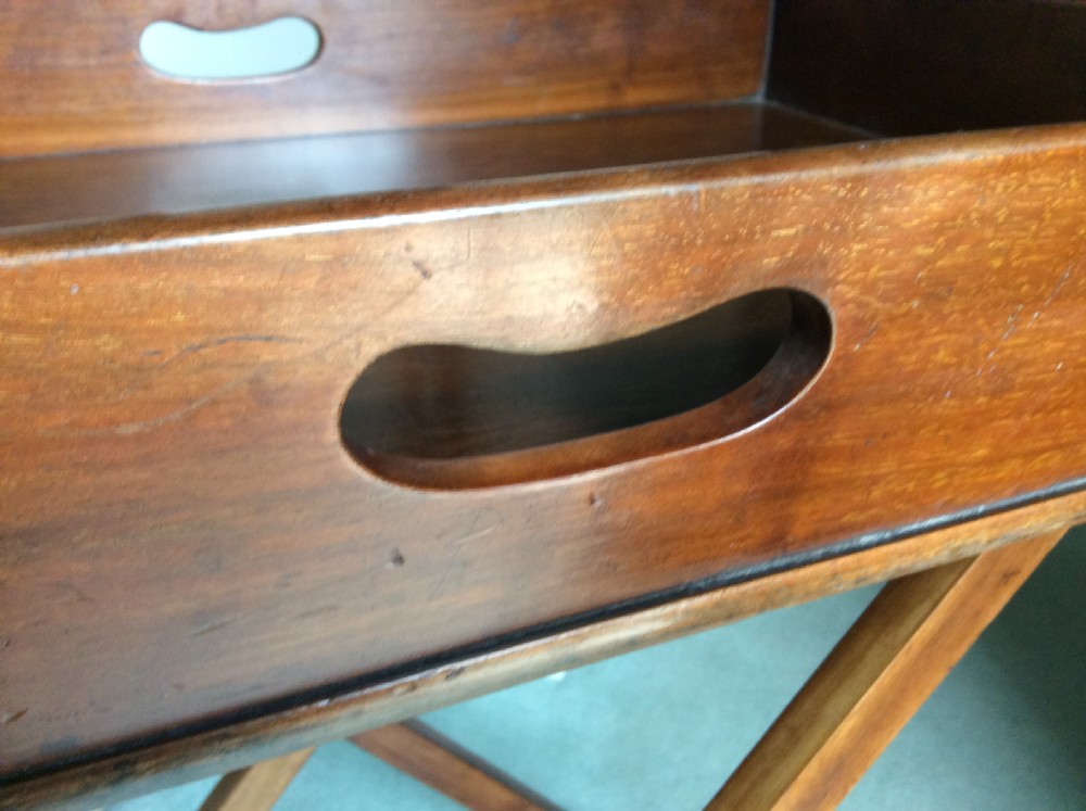 A nineteenth-century mahogany butlers tray featuring raised gallery sides with cut-out handles, resting on a folding X-frame wooden stand. View IV