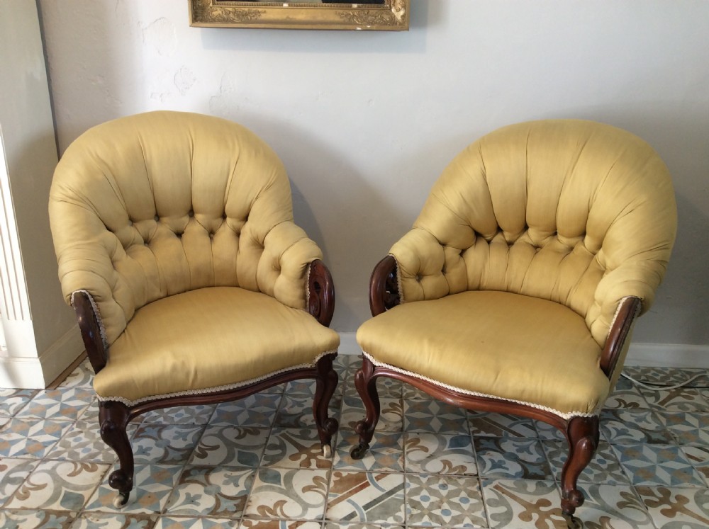 A near pair of Victorian button-backed tub armchairs upholstered in yellow fabric with carved mahogany cabriole legs on castors.