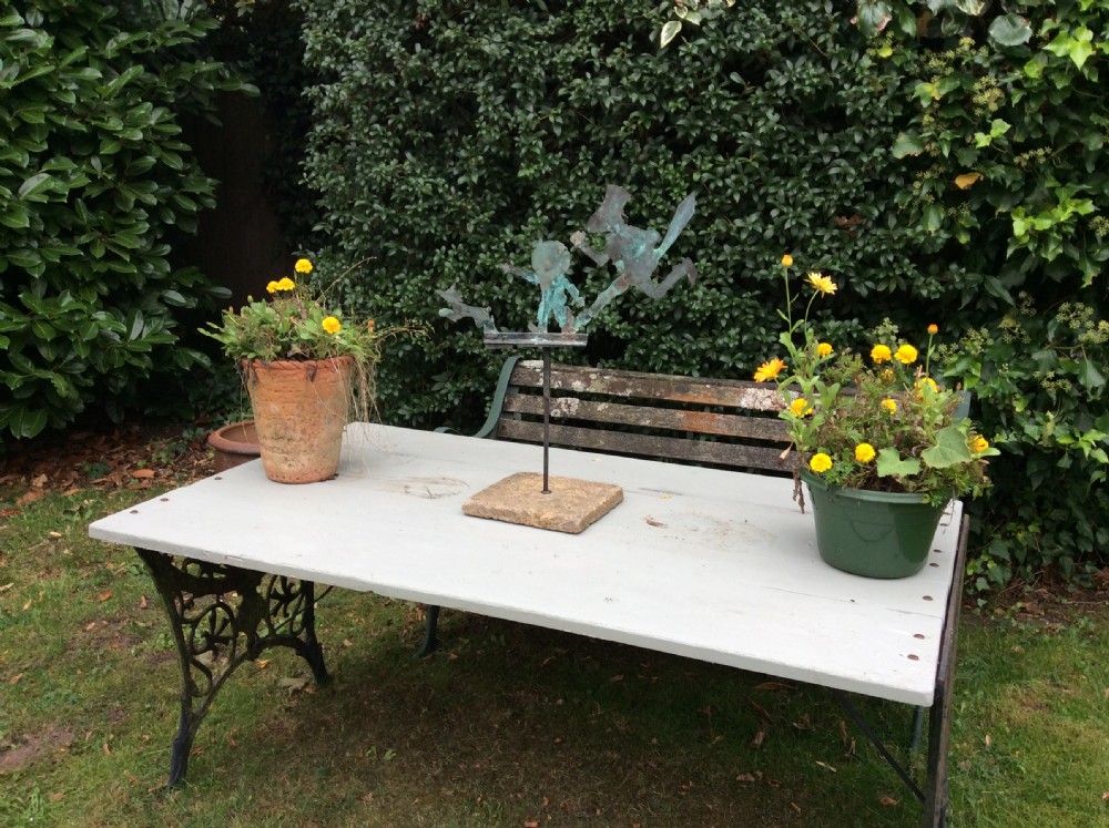 An early 20th-century copper weather vane featuring running figures with a natural verdigris patina, mounted on a stone block stand. View III