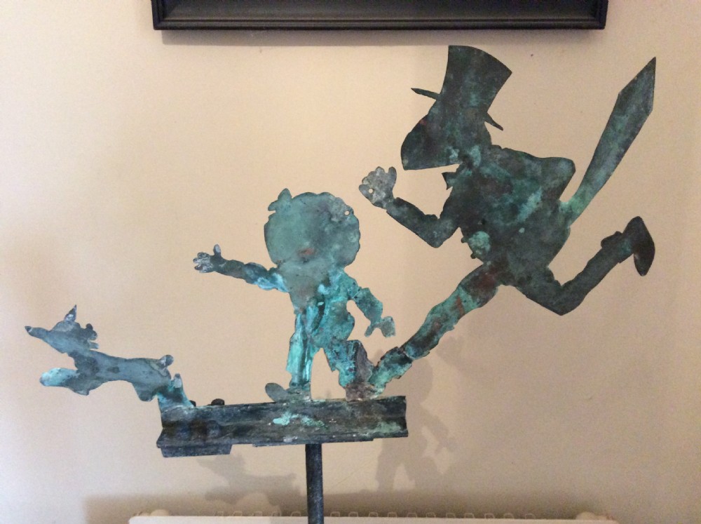 An early 20th-century copper weather vane featuring running figures with a natural verdigris patina, mounted on a stone block stand. View V