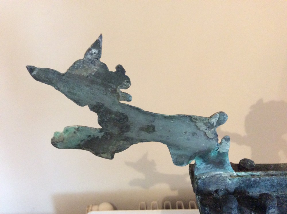 An early 20th-century copper weather vane featuring running figures with a natural verdigris patina, mounted on a stone block stand. View VII