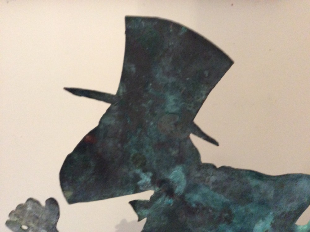 An early 20th-century copper weather vane featuring running figures with a natural verdigris patina, mounted on a stone block stand. View IX