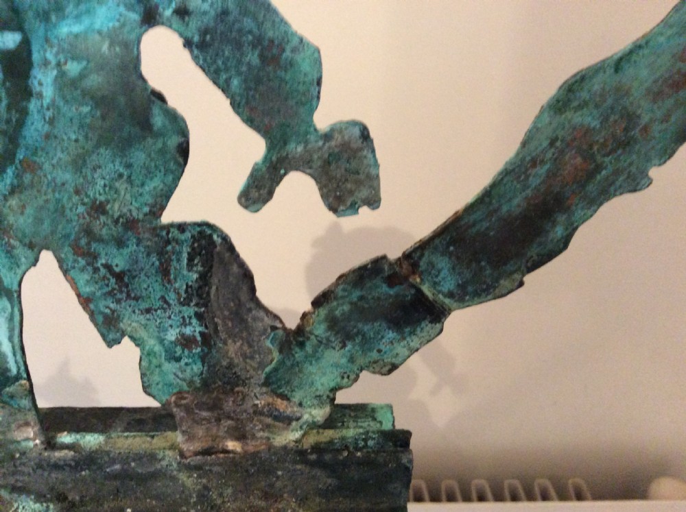 An early 20th-century copper weather vane featuring running figures with a natural verdigris patina, mounted on a stone block stand. View X
