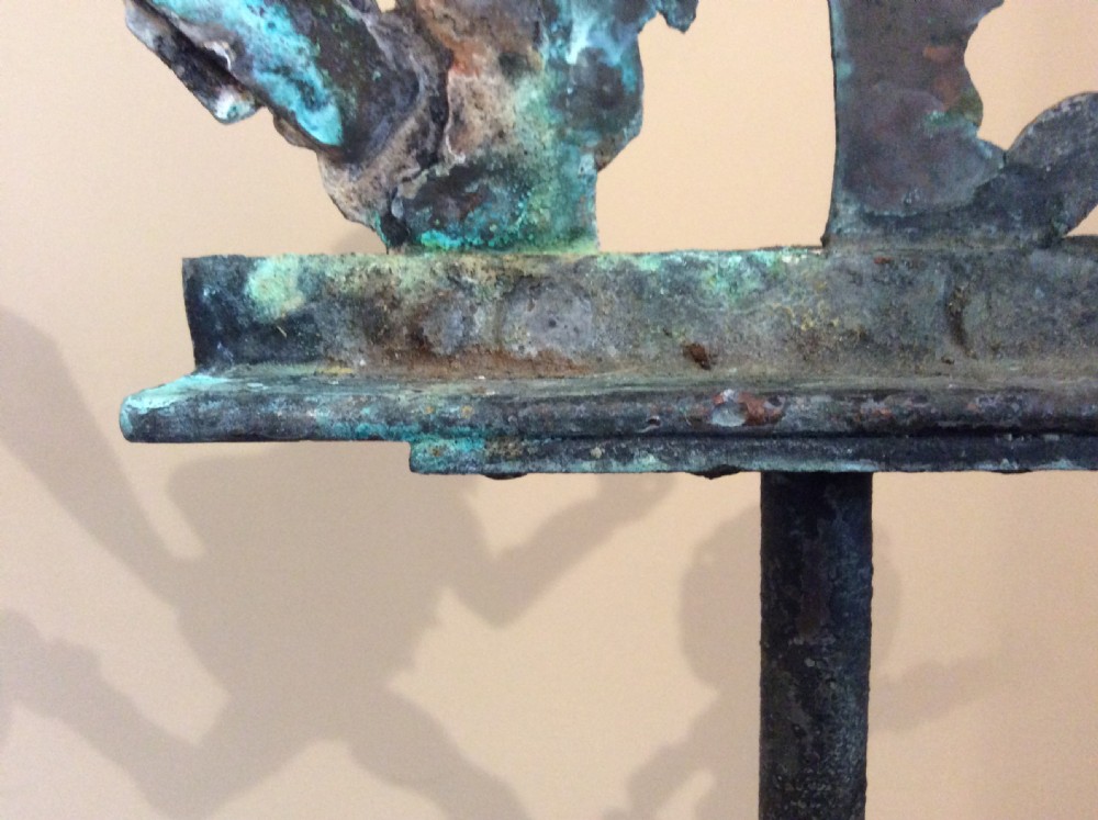 An early 20th-century copper weather vane featuring running figures with a natural verdigris patina, mounted on a stone block stand. View XVI
