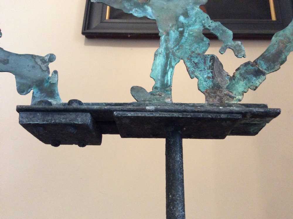 An early 20th-century copper weather vane featuring running figures with a natural verdigris patina, mounted on a stone block stand. View XIX