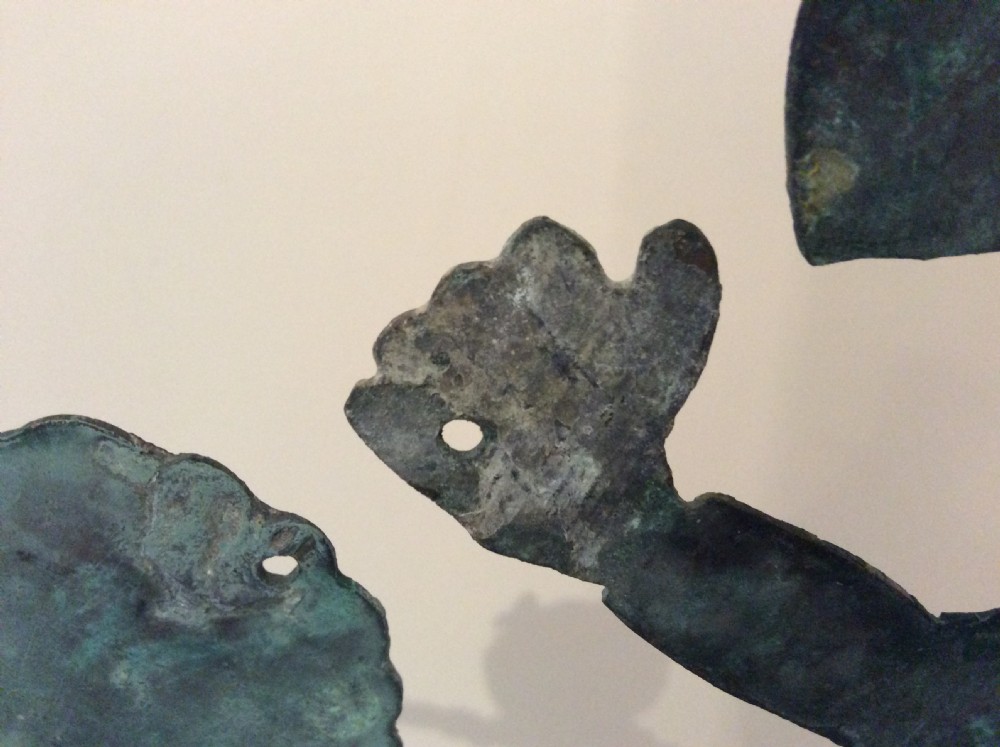 An early 20th-century copper weather vane featuring running figures with a natural verdigris patina, mounted on a stone block stand. View XXI