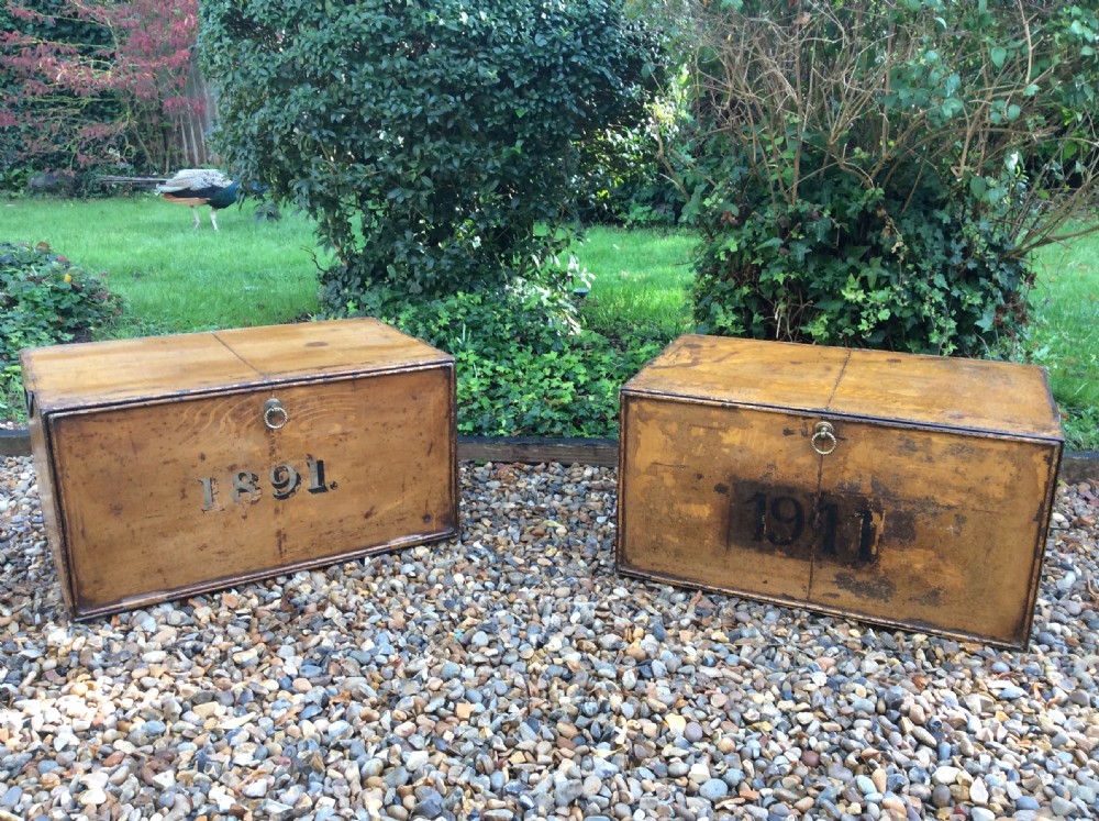 A pair of rectangular Victorian deed boxes finished in warm ochre paint with dark metal edging, ring pull handles, and black stencilled dates reading 1891 and 1911.