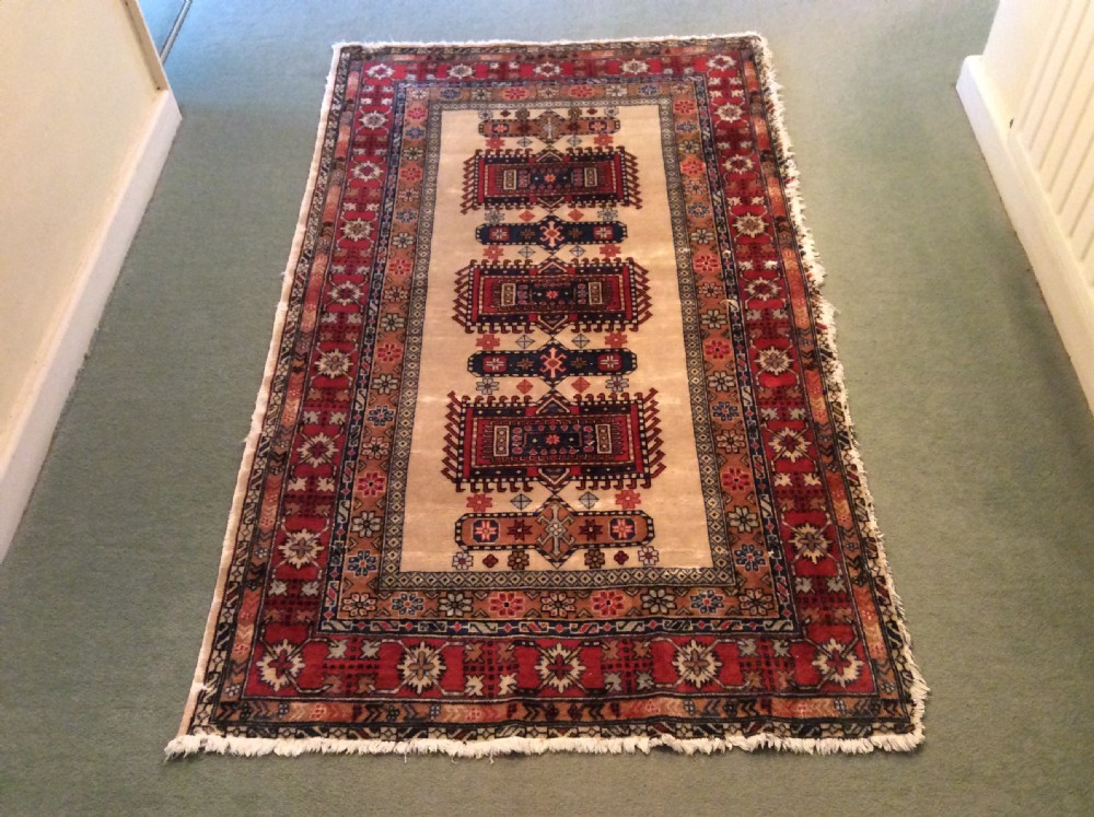 A small hand-woven antique Anatolian wool rug featuring geometric central medallions on a cream field surrounded by a patterned red and navy border.