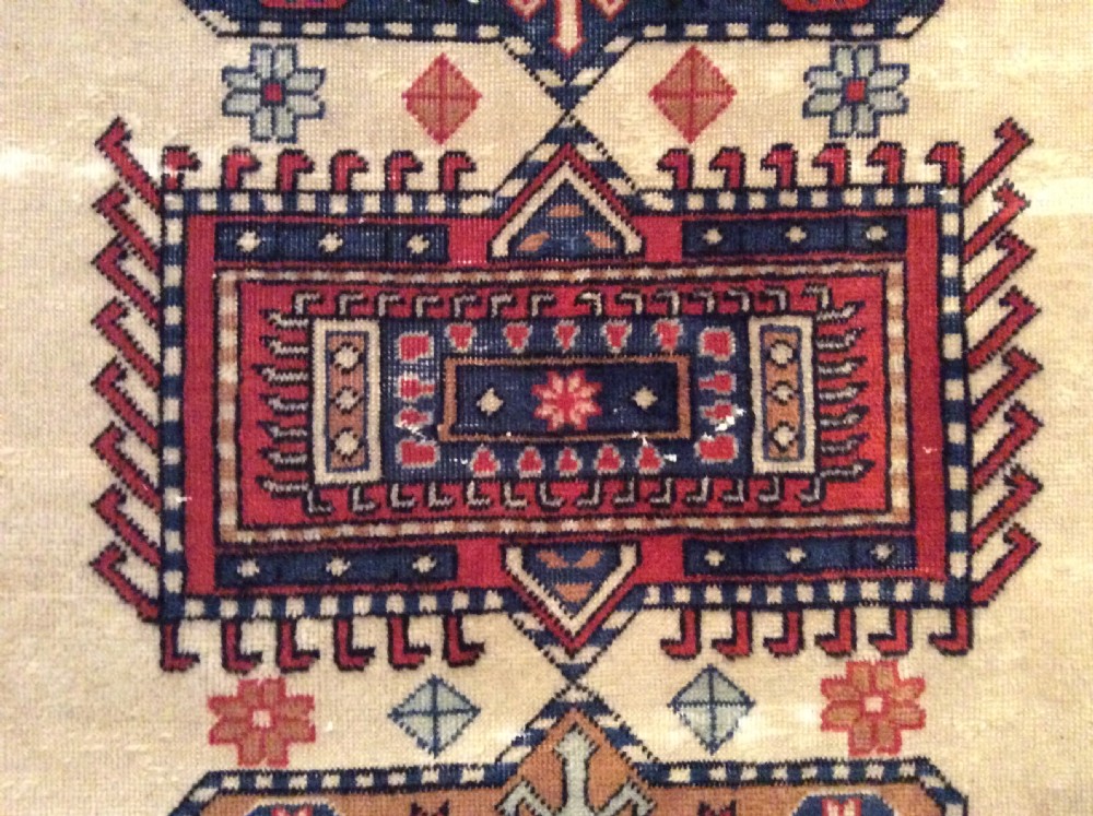 A small hand-woven antique Anatolian wool rug featuring geometric central medallions on a cream field surrounded by a patterned red and navy border. View III