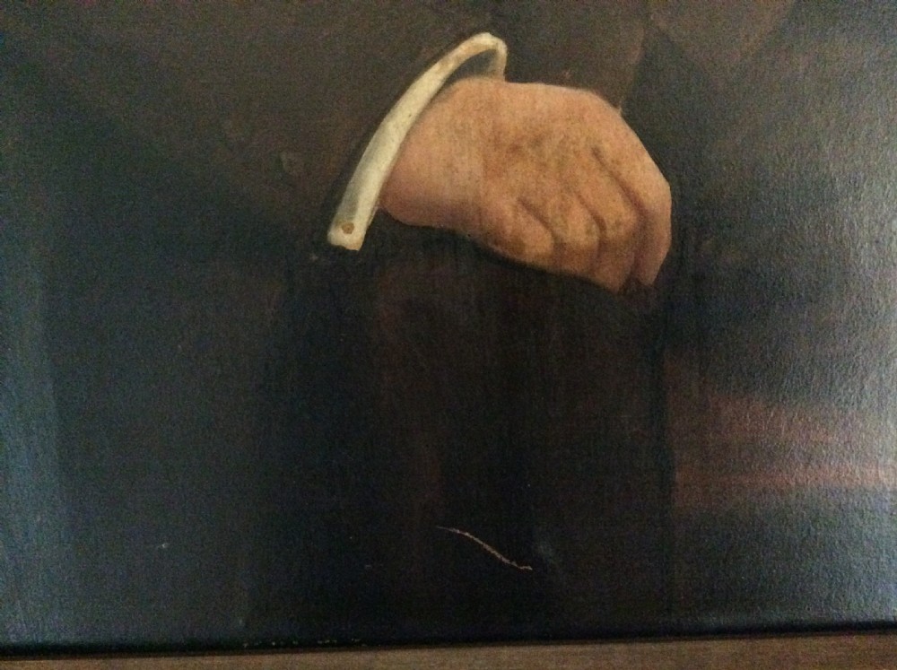 An antique oil painting depicting a seated gentleman in formal dark attire set within a heavily carved gold leaf frame. View V
