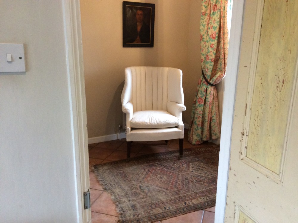 An antique George III high-backed barrel armchair upholstered in cream fabric with channel tufting, supported on dark mahogany legs with brass castors. View II