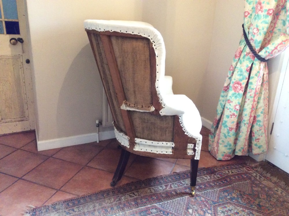 An antique George III high-backed barrel armchair upholstered in cream fabric with channel tufting, supported on dark mahogany legs with brass castors. View III