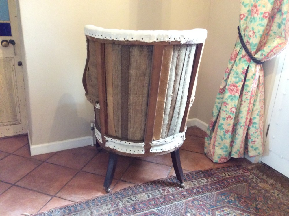 An antique George III high-backed barrel armchair upholstered in cream fabric with channel tufting, supported on dark mahogany legs with brass castors. View IV