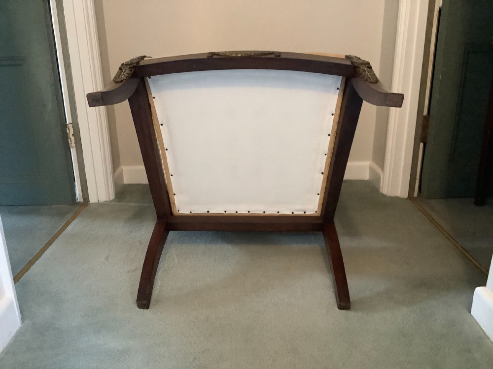 A 19th-century French Empire mahogany open armchair featuring light gold-coloured fabric upholstery and ornate brass leaf mounts. View X