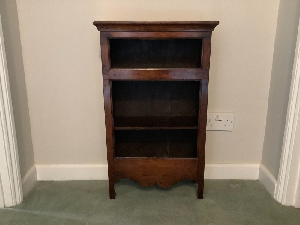 A small dark wood open French dwarf bookcase featuring three shelf tiers, a top moulded cornice, and a scalloped base apron.