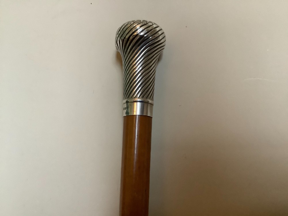 A wooden walking cane featuring a swirl-fluted hallmarked silver pommel top and silver collar.