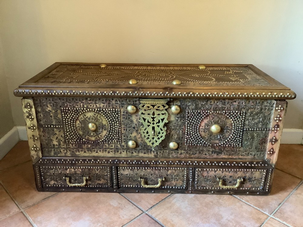 A nineteenth-century wooden Zanzibar storage chest decorated with intricate brass studs, pierced metal plates, three lower drawers, and brass handles.