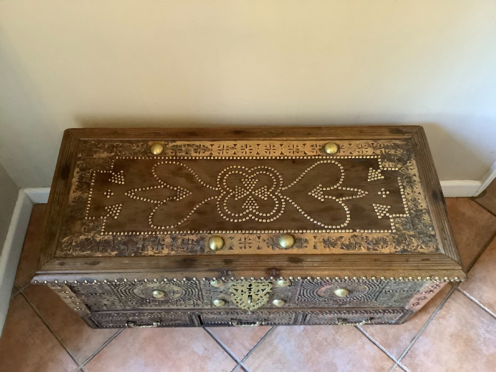 A nineteenth-century wooden Zanzibar storage chest decorated with intricate brass studs, pierced metal plates, three lower drawers, and brass handles. View V