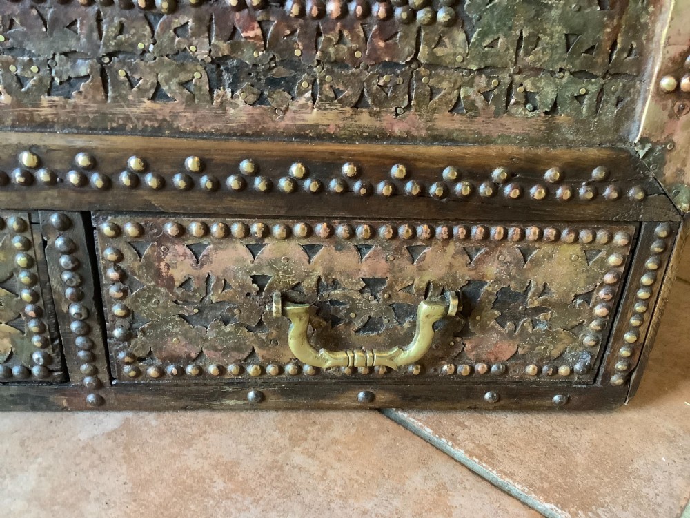 A nineteenth-century wooden Zanzibar storage chest decorated with intricate brass studs, pierced metal plates, three lower drawers, and brass handles. View VI