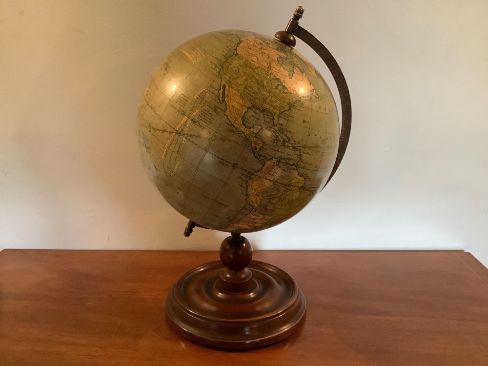 An antique terrestrial desk globe featuring printed paper gores, a brass semi-meridian arc, and a dark turned wooden base.