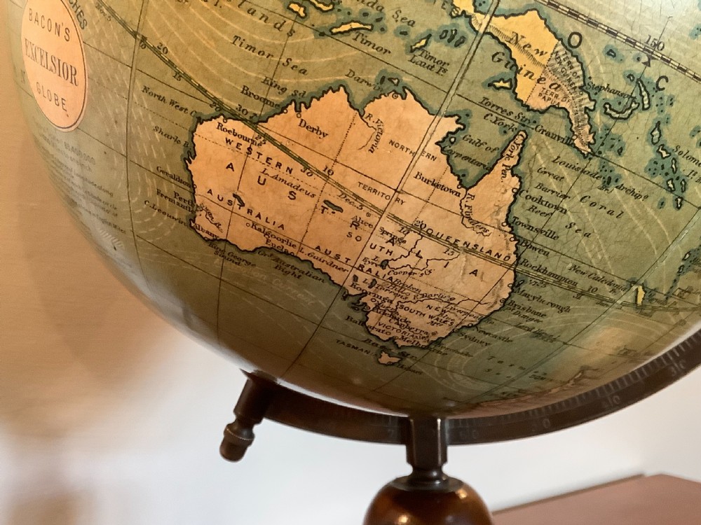 An antique terrestrial desk globe featuring printed paper gores, a brass semi-meridian arc, and a dark turned wooden base. View X