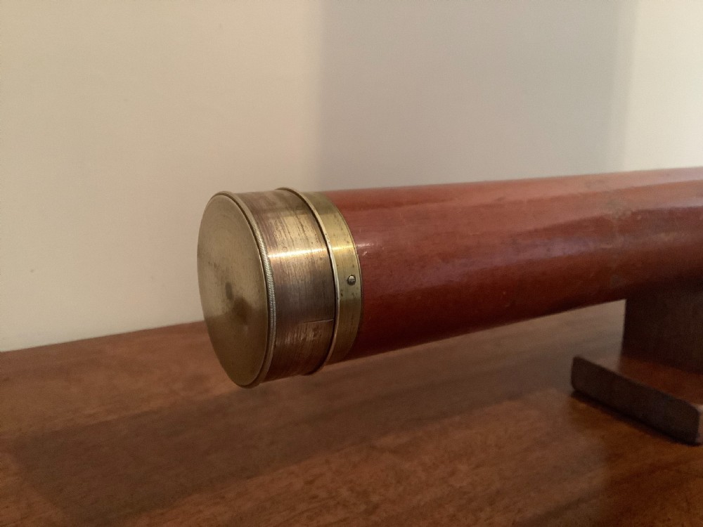 An antique brass multi-draw telescope with a leather-bound barrel rested horizontally on a fitted wooden display stand. View III