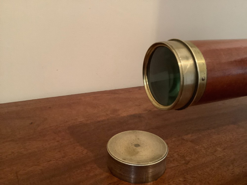 An antique brass multi-draw telescope with a leather-bound barrel rested horizontally on a fitted wooden display stand. View V