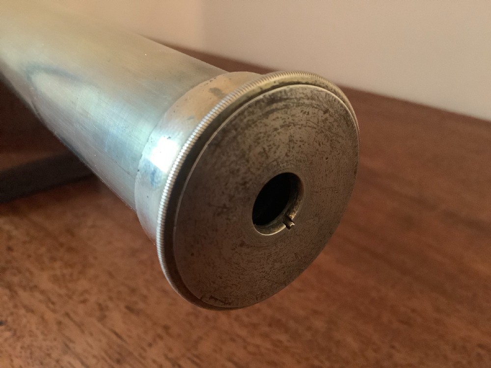 An antique brass multi-draw telescope with a leather-bound barrel rested horizontally on a fitted wooden display stand. View VII