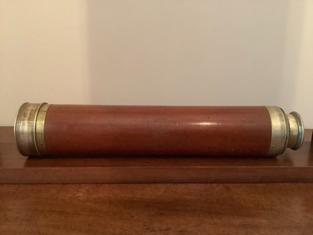 An antique brass multi-draw telescope with a leather-bound barrel rested horizontally on a fitted wooden display stand. View VIII