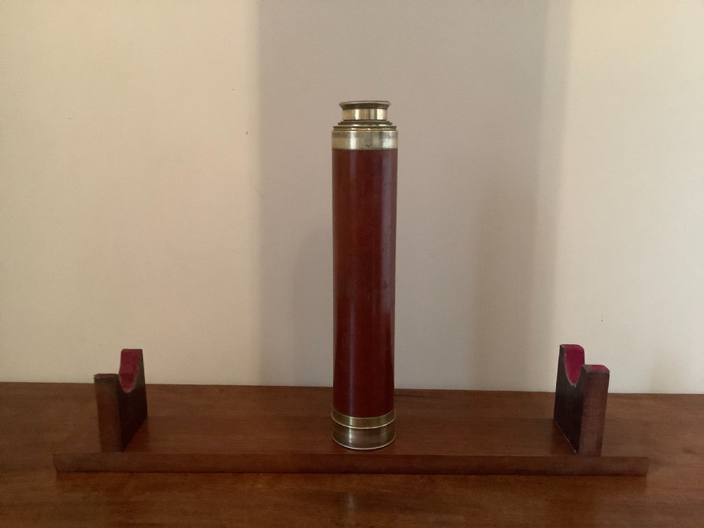 An antique brass multi-draw telescope with a leather-bound barrel rested horizontally on a fitted wooden display stand. View IX