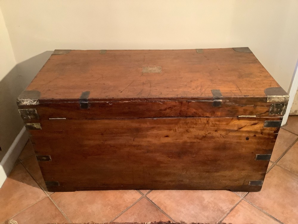 A rectangular warm brown camphor wood campaign trunk featuring corner brass brackets, flush brass straps, and a central brass ring handle. View XI