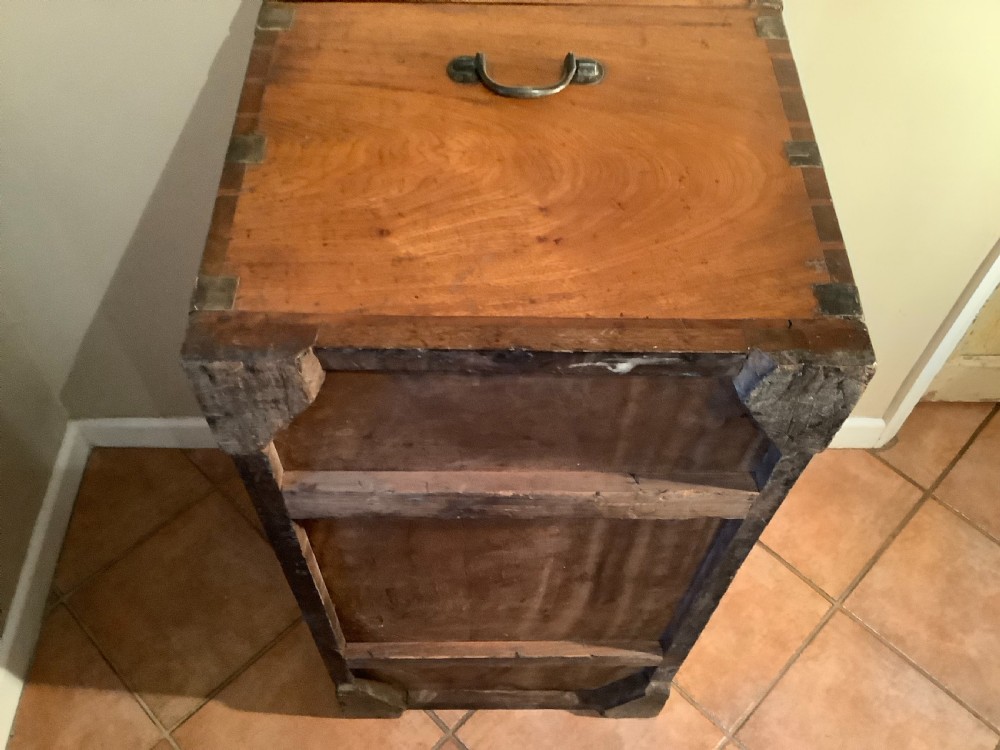A rectangular warm brown camphor wood campaign trunk featuring corner brass brackets, flush brass straps, and a central brass ring handle. View XII