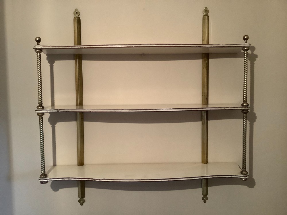 A three-tier off-white painted wood wall shelf unit featuring turned spiral brass side supports and vertical mounting rails.