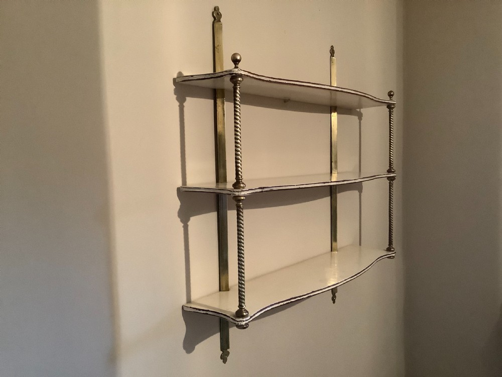 A three-tier off-white painted wood wall shelf unit featuring turned spiral brass side supports and vertical mounting rails. View VII