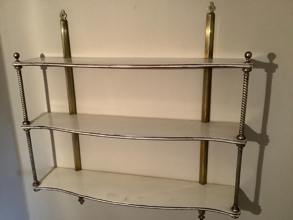 A three-tier off-white painted wood wall shelf unit featuring turned spiral brass side supports and vertical mounting rails. View VIII