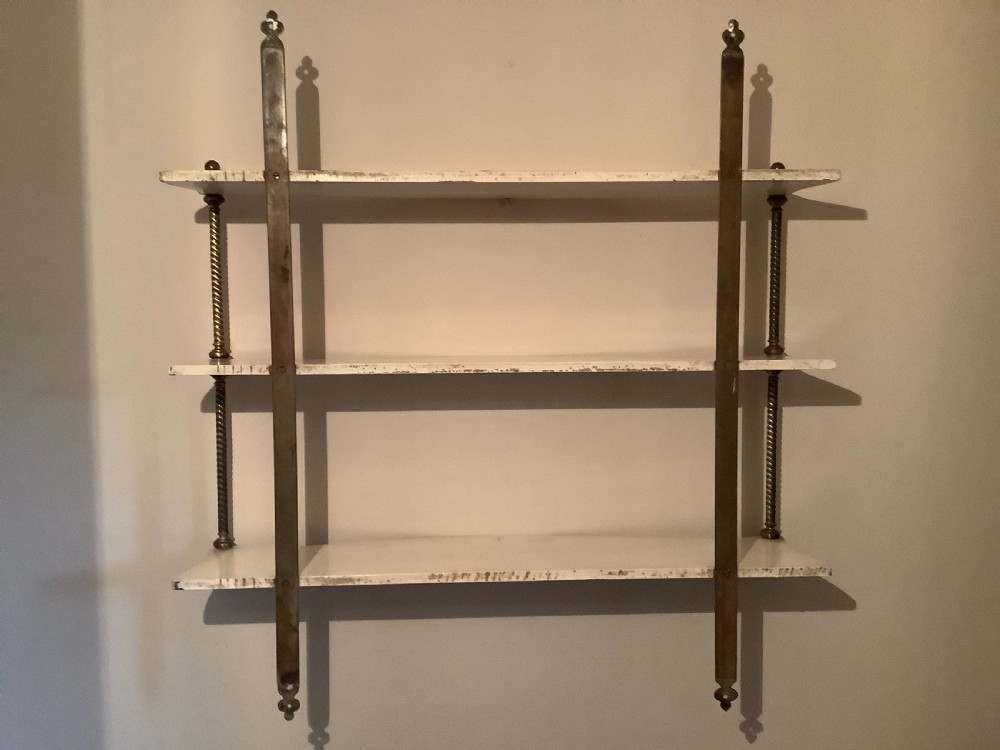 A three-tier off-white painted wood wall shelf unit featuring turned spiral brass side supports and vertical mounting rails. View X