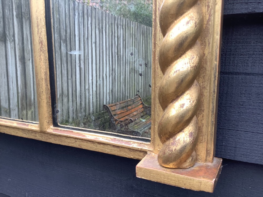 A 19th-century giltwood triple plate overmantel mirror featuring spiral-twist side columns, a dark painted frieze with gold rosettes, and a central carved shell motif. View VI