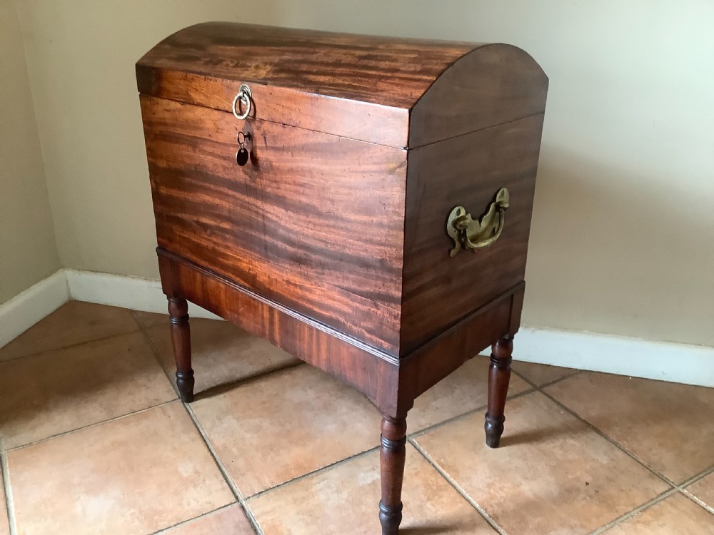 A Georgian mahogany cellarette featuring a domed lid, turned legs, flame mahogany wood grain, and side brass handles.